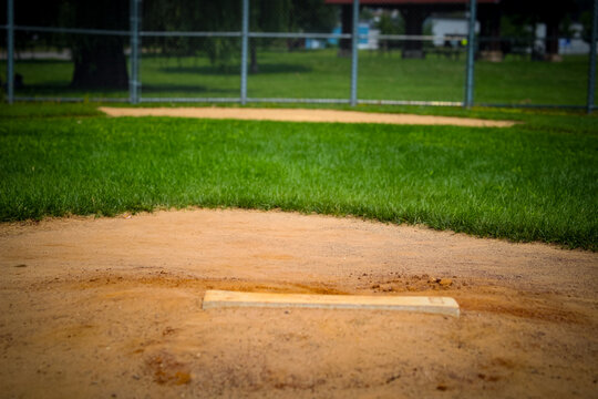 a baseball field, featuring a base in the foreground and the infield dirt and grass leading towards the outfield in the background. sports and recreation or dedication concept with copy space