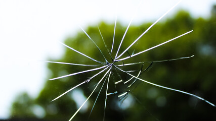 shattered glass on a window glass or windshield with radiating cracks. abstract texture and outdoor...