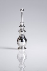 Fototapeta premium Shiny silver ornamental object featuring a bulbous base, slender neck, and a small sphere on top, reflecting on a sleek surface