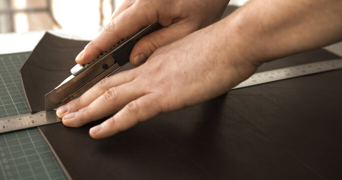 Cutting leather with utility knife and ruler in professional leathercraft workshop
