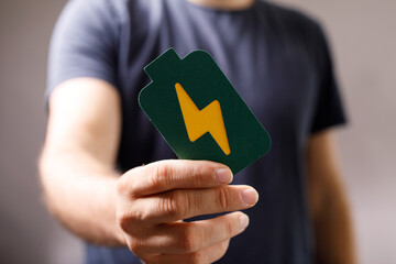 Close-up of a man's hand holding a green card with a yellow lightning bolt, symbolizing energy,...