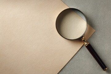 Vintage magnifying glass with a dark handle resting on a blank sheet of textured beige paper with copy space.