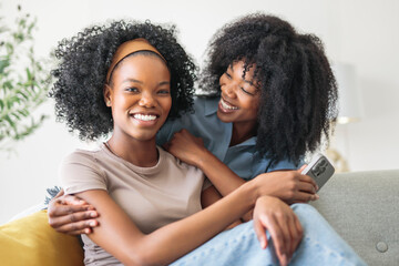 black mother and daughter using cellphone on sofa