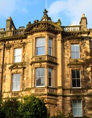 Naklejka premium Ornate stone building facade, with large windows and decorative details, set against a partly cloudy sky