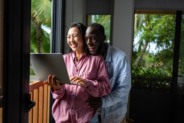Happy young diverse, multiethnic couple planning budget, reading good news on laptop at home