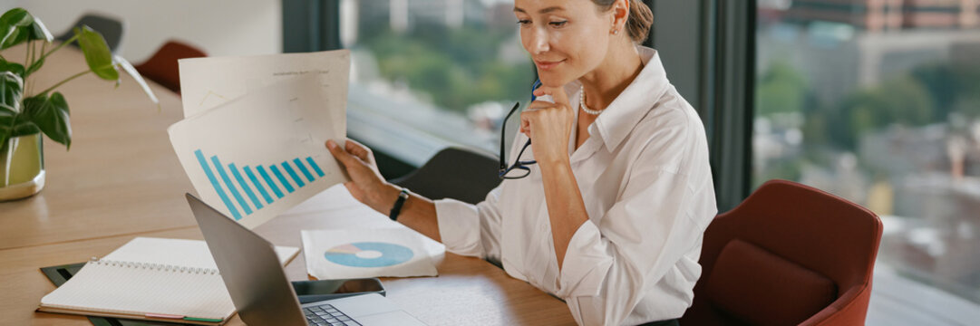 A confident businesswoman is analyzing growth data meticulously in a modern office space - Powered by Adobe