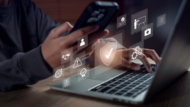 Close-up of hands using laptop and smartphone with digital interface icons symbolizing workplace security, digital governance, compliance monitoring, and risk control in a modern tech environment.