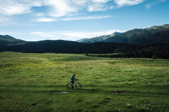 Aerial view of woman cyclist riding mountain bike on flowering grassland mountain - Powered by Adobe