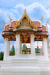 Naklejka premium Wat Rakhang temple pavilion in Bangkok, Thailand. White columns and golden Thai motifs frame hanging pastel blue green bells under bright blue sky, iconic Buddhist landmark.