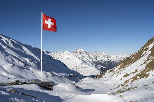 Swiss flag in front of mountain landscape in winter, mountain panorama with the peaks of the Berg&uuml;ner St&ouml;cke Tinzenhorn and Piz Ela, view at the Keschh&uuml;tte in winter, B&uuml;ndner Haute Route, Albula Alps, Rhaetian Alps, Grisons, Eastern Switzerland, Switzerland