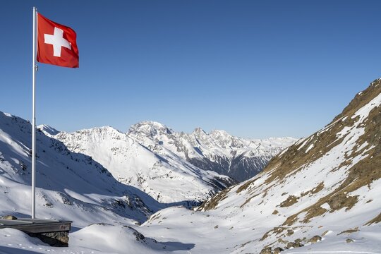 Swiss flag in front of mountain landscape in winter, mountain panorama with the peaks of the Berg&uuml;ner St&ouml;cke Tinzenhorn and Piz Ela, view at the Keschh&uuml;tte in winter, B&uuml;ndner Haute Route, Albula Alps, Rhaetian Alps, Grisons, Eastern Switzerland, Switzerland