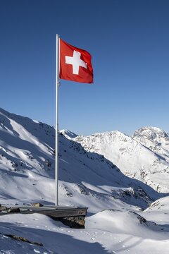 Swiss flag in front of mountain landscape in winter, mountain panorama with the peaks of the Berg&uuml;ner St&ouml;cke Tinzenhorn and Piz Ela, view at the Keschh&uuml;tte in winter, B&uuml;ndner Haute Route, Albula Alps, Rhaetian Alps, Grisons, Eastern Switzerland, Switzerland