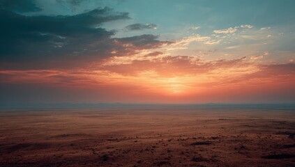 Vibrant sunset over a vast, flat, arid landscape with hazy mountains in the distance and a blend of orange, red, and blue hues in the sky