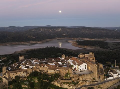 The White Village of Castillo de Castellar is located inside a Moorish castle. High above the reservoir Guadarranque. With full moon at dawn. Aerial view. Drone shot. C&aacute;diz province, Andalusia, Spain