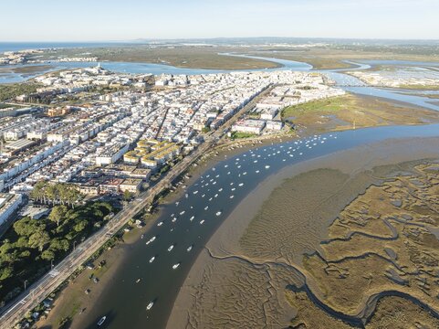 The town of Isla Cristina adjacent to the Carreras river with fishing boats and its marshland at low tide. Aerial view. Drone shot. Huelva province, Andalusia, Spain