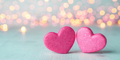 Obraz premium Two sweet pink heart shaped macarons sit side by side on a light blue surface with a soft bokeh background of warm golden lights creating a romantic and celebratory atmosphere