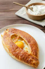 Adjarian khachapuri with egg yolk on a gray plate on a wooden table in the kitchen. The concept of traditional Georgian pastries. Vertical orientation.