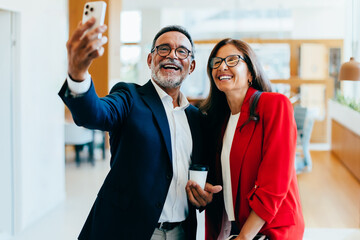 Two senior managers smiling while taking a smartphone selfie together