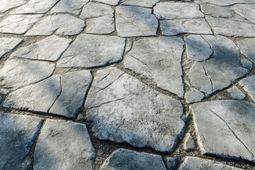 Detailed close up of gray irregular stone pavement. Rough weathered outdoor concrete surface with cracks and unique natural rock texture.