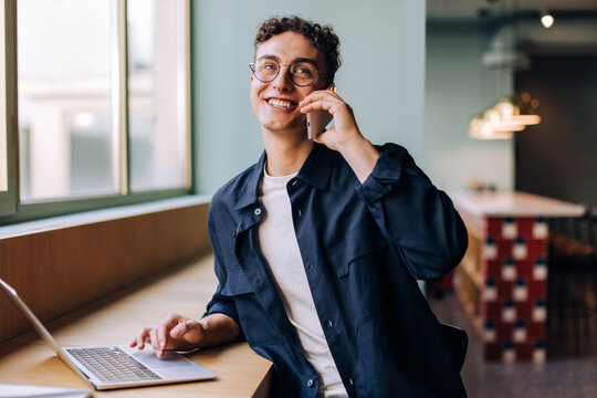 Smiling young professional man on a phone call while using a laptop - Powered by Adobe