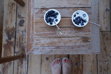 Top view of two bowls with fresh blueberries on a wooden table. Out of focus feet with red nail...