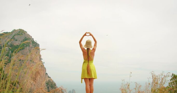 Woman making heart shape with hands on cliffside during summer Capri hiking tour