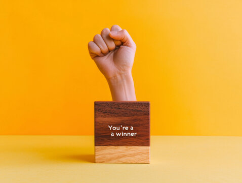 Triumphant fist emerges from wooden block proclaiming, You're a winner