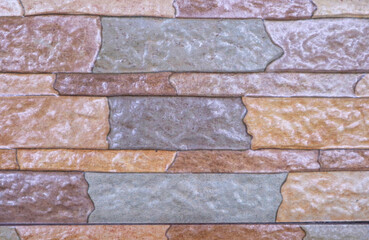 A detailed, full-frame shot of a modern, multi-colored brick or stone tile wall. The textured surface features a repeating pattern of rectangular blocks in various shades
