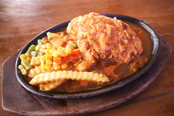 A sizzling hot plate of fried chicken with gravy, fries, corn, carrots, beans, and onions, symbolizing delicious comfort food and hearty dining.