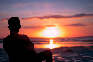 A solitary individual sits on the edge of the land, silhouetted against an intensely vibrant...
