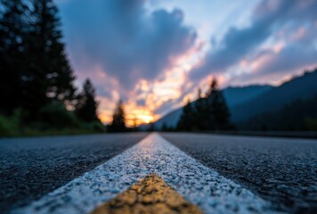 Road vanishing to mountain sunset. White line guide through blurry trees as golden light breaks over peaks, textured asphalt in foreground