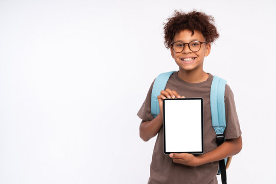 Smiling African-American school preteen boy elementary primary pupil holding using digital tablet for e-learning showing demonstrate mock up empty screen isolated over white background copy space - Powered by Adobe