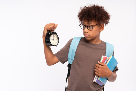 Socked African-American preteen boy male elementary primary pupil with bag holding looking on round clock worried about time harry up isolated over white background. Education back to school concept