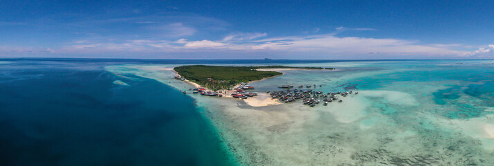 Aerial view of sea gypsy village over clear turquoise waters in Omadal Island Semporna, Sabah, Malaysia. Scenic seascape with coral reefs, coastal village, and blue tropical sky.