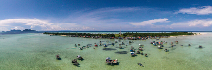 Aerial view of sea gypsy village over clear turquoise waters in Kulapuan Island Semporna, Sabah, Malaysia. Scenic seascape with coral reefs, coastal village, and blue tropical sky.