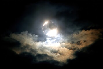 Solar eclipse shines with 'diamond ring' effect seen through atmospheric clouds, illuminating the ethereal sky