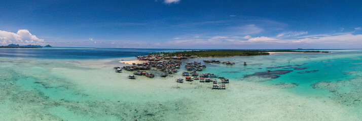 Aerial view of sea gypsy village over clear turquoise waters in Omadal Island Semporna, Sabah, Malaysia. Scenic seascape with coral reefs, coastal village, and blue tropical sky.