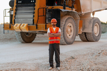 Confident construction worker posing with crossed arms in front of dumper truck