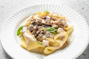 Pappardelle pasta with creamy mushroom sauce, garnished with basil and chili flakes, served on a white plate. Top view, rustic presentation, ideal for gourmet food themes