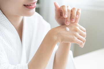 Health care, beauty smile pretty asian young woman in bathrobe, towel after shower bath at home, finger applying moisturizer on her back hand. Skin body cream moisturizing lotion, routine in morning.
