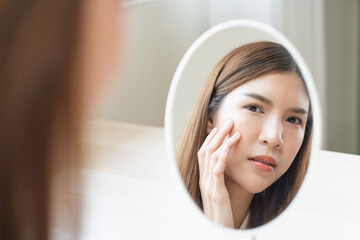 Anti aging, worry puberty asian young woman, stressed girl looking in mirror, allergy presenting an allergic reaction from cosmetic on face. Beauty, health care from acne problem, dry skin, treatment.