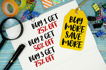 Buy 1 get 25%, Buy 2 get 50%, Buy 3 get 75% text on a notepad paper and Buy More Save More with price tag surrounded by office supplies and magnifying glass on a blue wooden surface