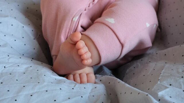 Slow-motion closeup of infant feet in pink pajamas gently moving on a soft blanket.