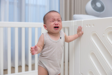 Upset baby crying and standing in playpen