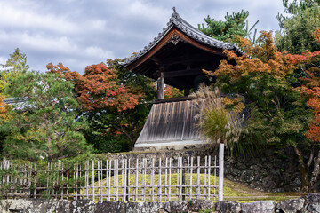 Wooden belfry framed by red maples and bamboo fencing stands quietly in Tenryu-ji, Kyoto, capturing autumn and the essence of temple serenity