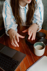 A person is animatedly speaking while working on a laptop at a coffee shop. They are gesturing with their hands, showing enthusiasm for the discussion. A cup of coffee and headphones are nearby.