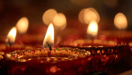 Diwa;i- Close-up of colorful, intricately painted diyas with flickering flames casting warm golden light, highlighted by soft bokeh and shallow focus, celebrating Diwali’s spirit of light, beauty