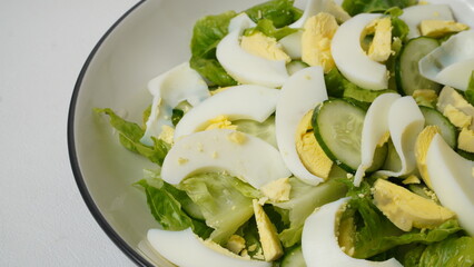 A serving of salad consisting of sliced ​​romaine lettuce, Japanese cucumber (kyuri), and boiled egg  without salad dressing served on a white plate and white background.