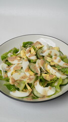 A serving of salad consisting of sliced ​​romaine lettuce, Japanese cucumber (kyuri), and boiled egg then topped with roasted sesame salad dressing served on a white plate and white background.