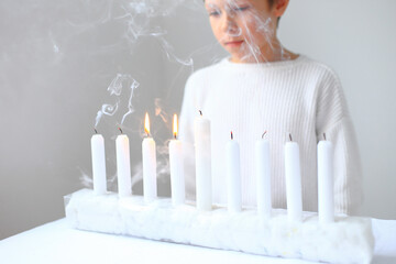 a child joyfully celebrating Hanukkah, surrounded by glowing candles. The warm light of the menorah...